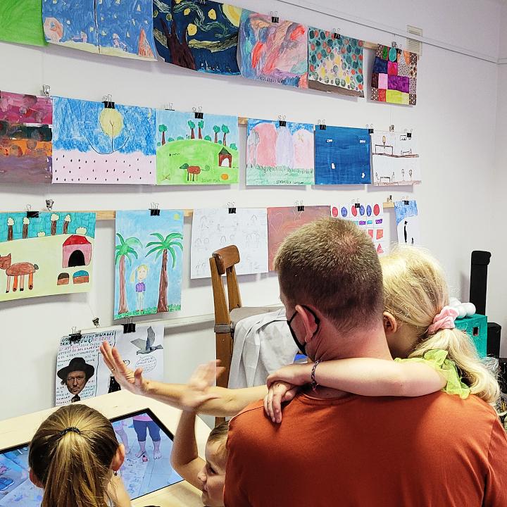 rodzice ogladaja wystawe obrazow dzieci z warsztatow wakacyjnych